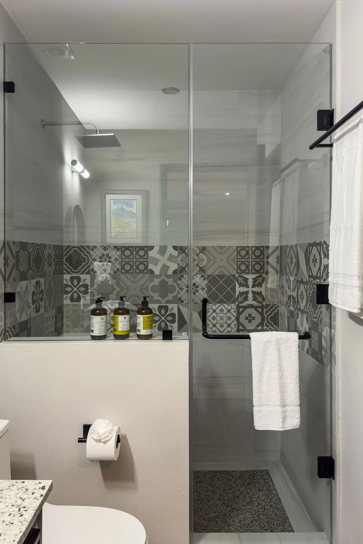 A bathroom with a glass shower and a band of patterned tile.