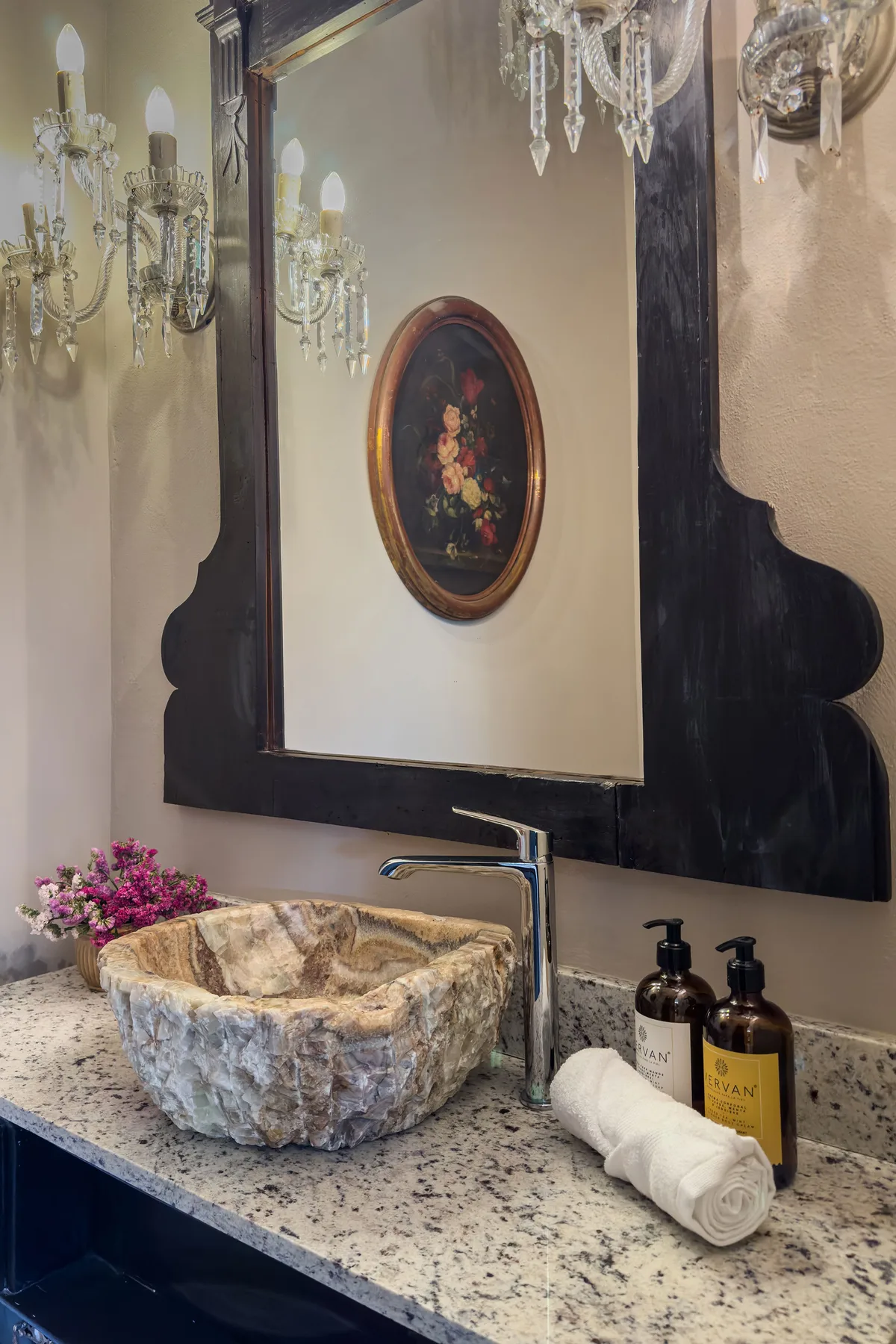 A bathroom vanity with a stone vessel sink, wall mirror, and folded towels.