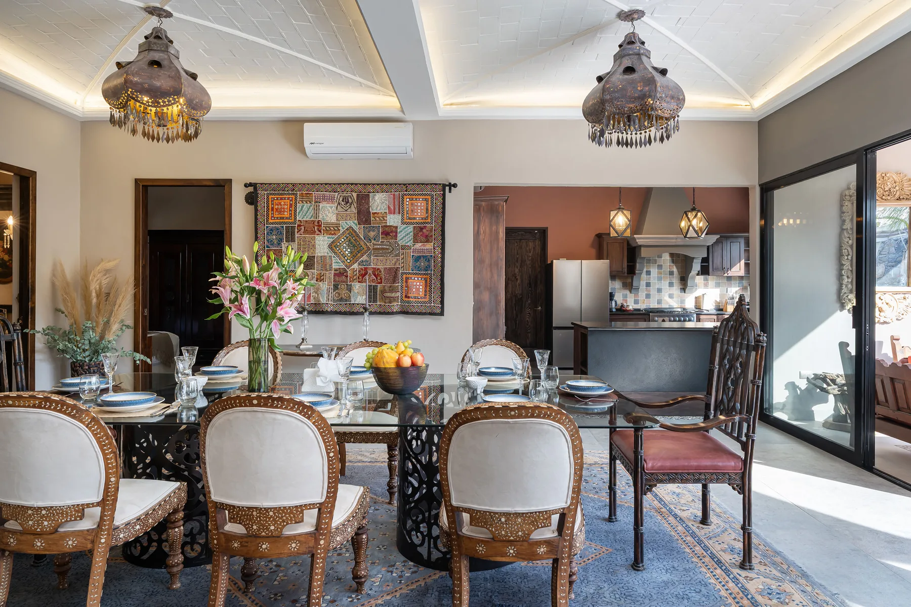 A dining area with a glass table, upholstered chairs, and a compact kitchen beyond.