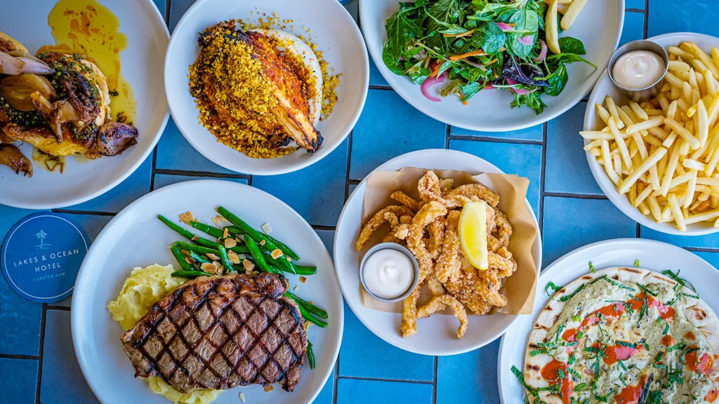 Espacio representativo del hotel: Una mesa muestra varios platos servidos, como carne a la parrilla, ensalada, papas fritas y pizza.