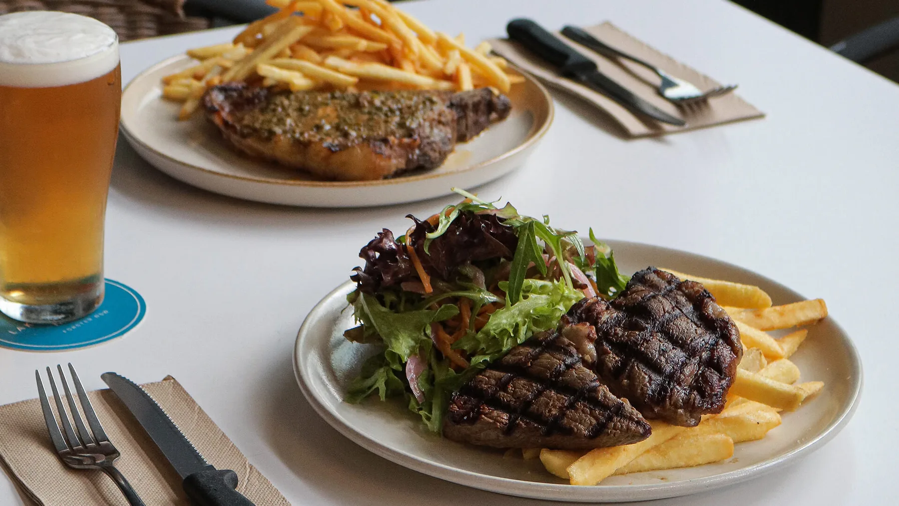 Espacio representativo del hotel: Una mesa de restaurante con carne a la parrilla, papas fritas, ensalada y un vaso de cerveza.