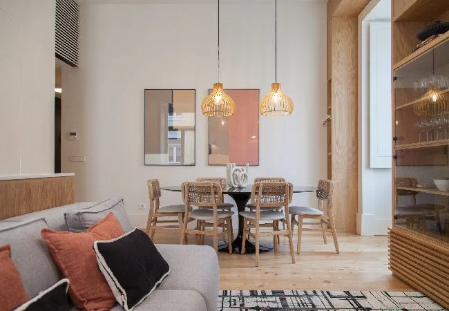 A dining area with a wooden table and pendant lights beside a living area.