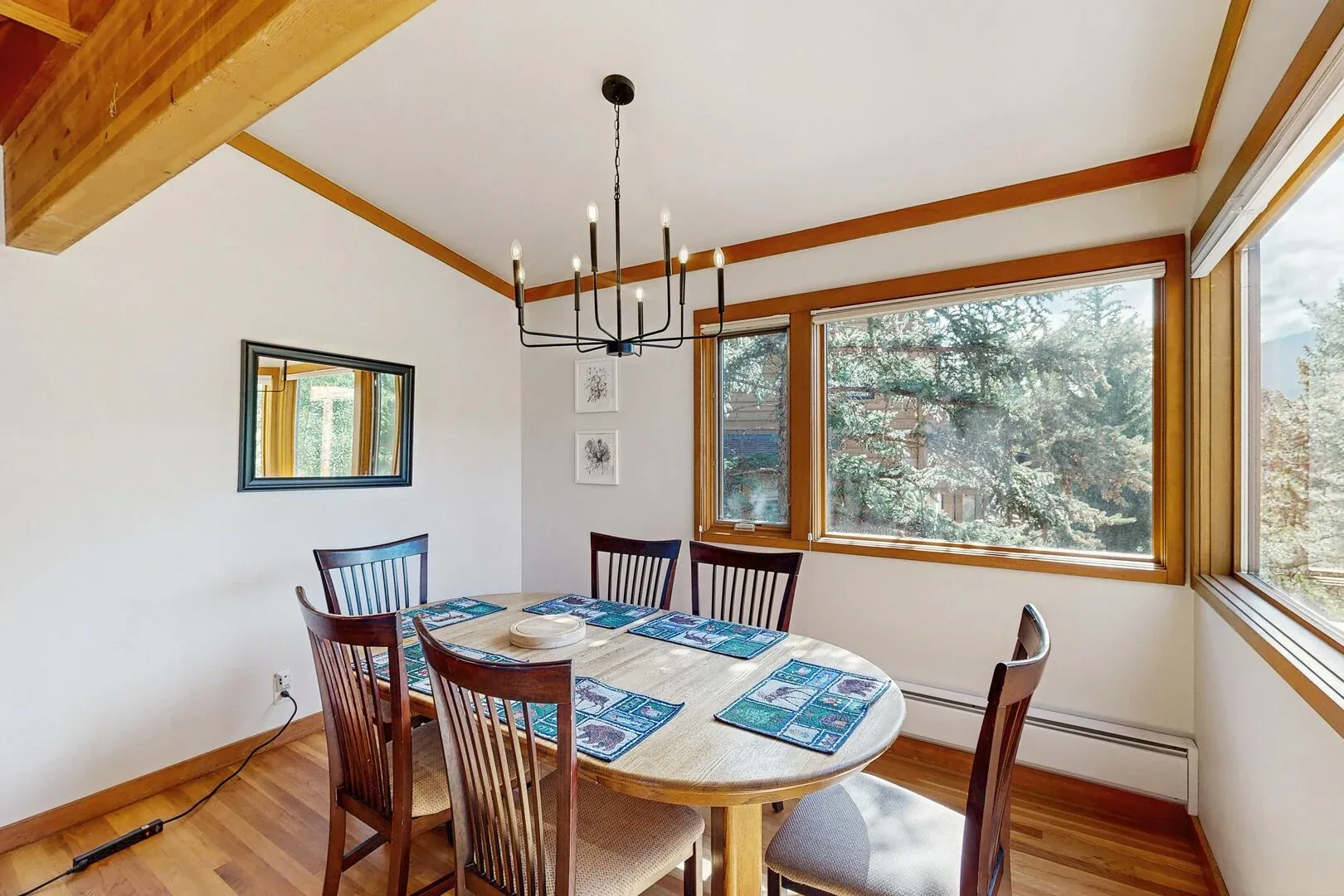 A dining area with a wooden table beneath a chandelier, beside large windows.