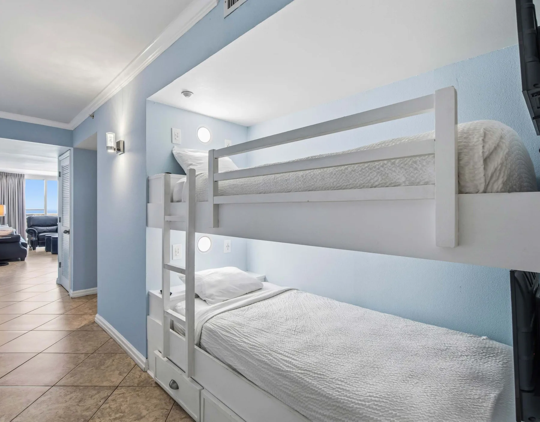 Zona para dormir con literas, paredes celestes y ropa de cama blanca.