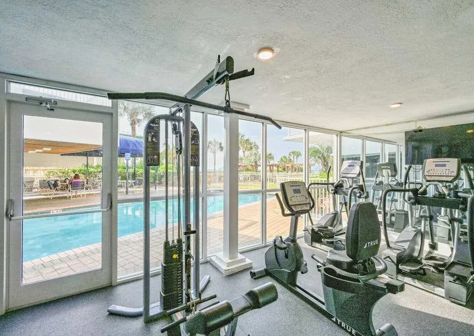 Zona común: Un gimnasio con máquinas de ejercicio junto a grandes ventanas con vistas a una piscina exterior.