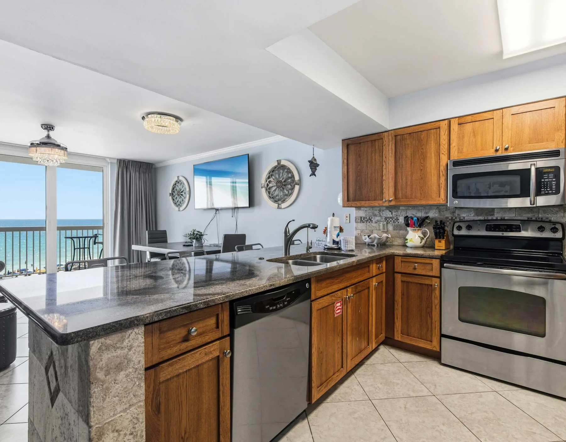 Una cocina con gabinetes de madera y una encimera da a un comedor y a una vista al mar.