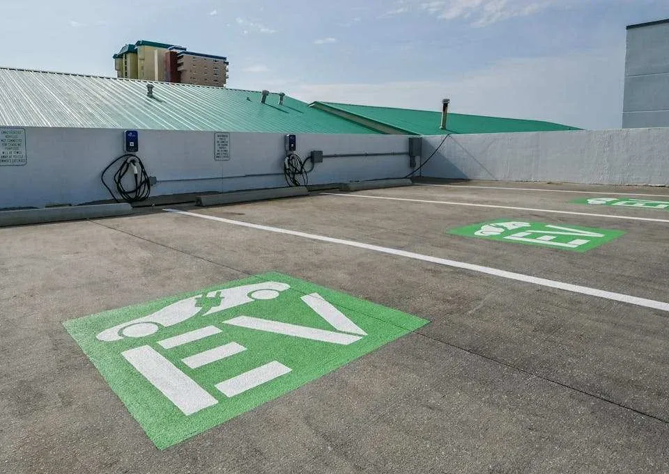 Zona común: Zona de estacionamiento con símbolos verdes de carga para vehículos eléctricos pintados en el pavimento.