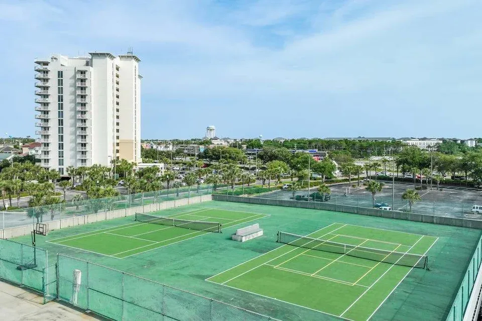 Zona común: Las canchas de tenis al aire libre están rodeadas de malla verde junto a un edificio alto.