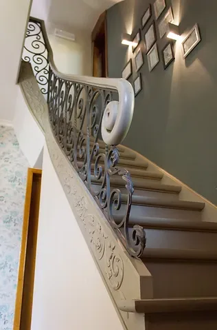 Espacio representativo del hotel: Una escalera curva con barandales ornamentados sube junto a cuadros en la pared.