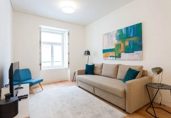 Una sala luminosa con un sofá beige, asientos azules y arte colorido en la pared.