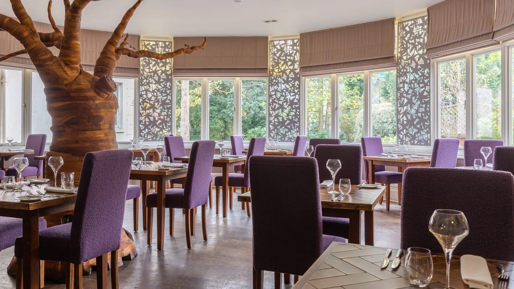 Representative hotel space: A dining room with tables and purple upholstered seating beside large windows.
