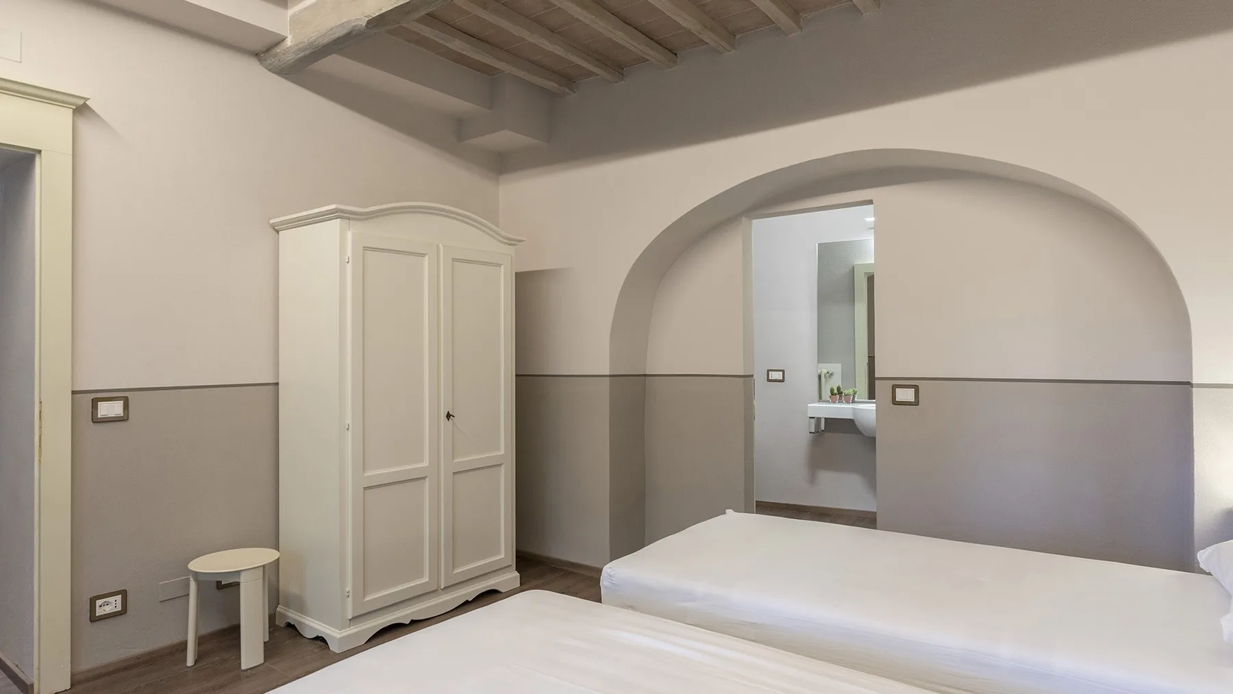 Un dormitorio con una cama blanca, un armario y un arco que da a un baño.