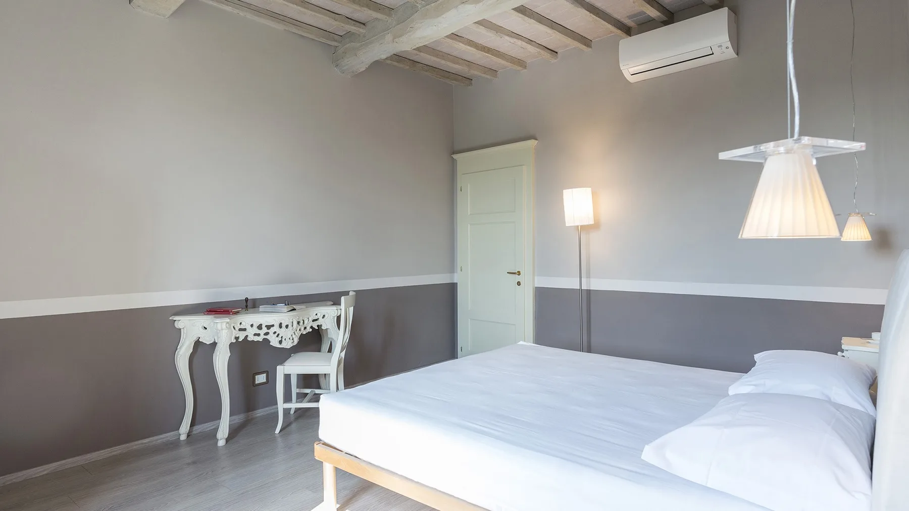 Un dormitorio con una cama, un escritorio pequeño y vigas expuestas en el techo.
