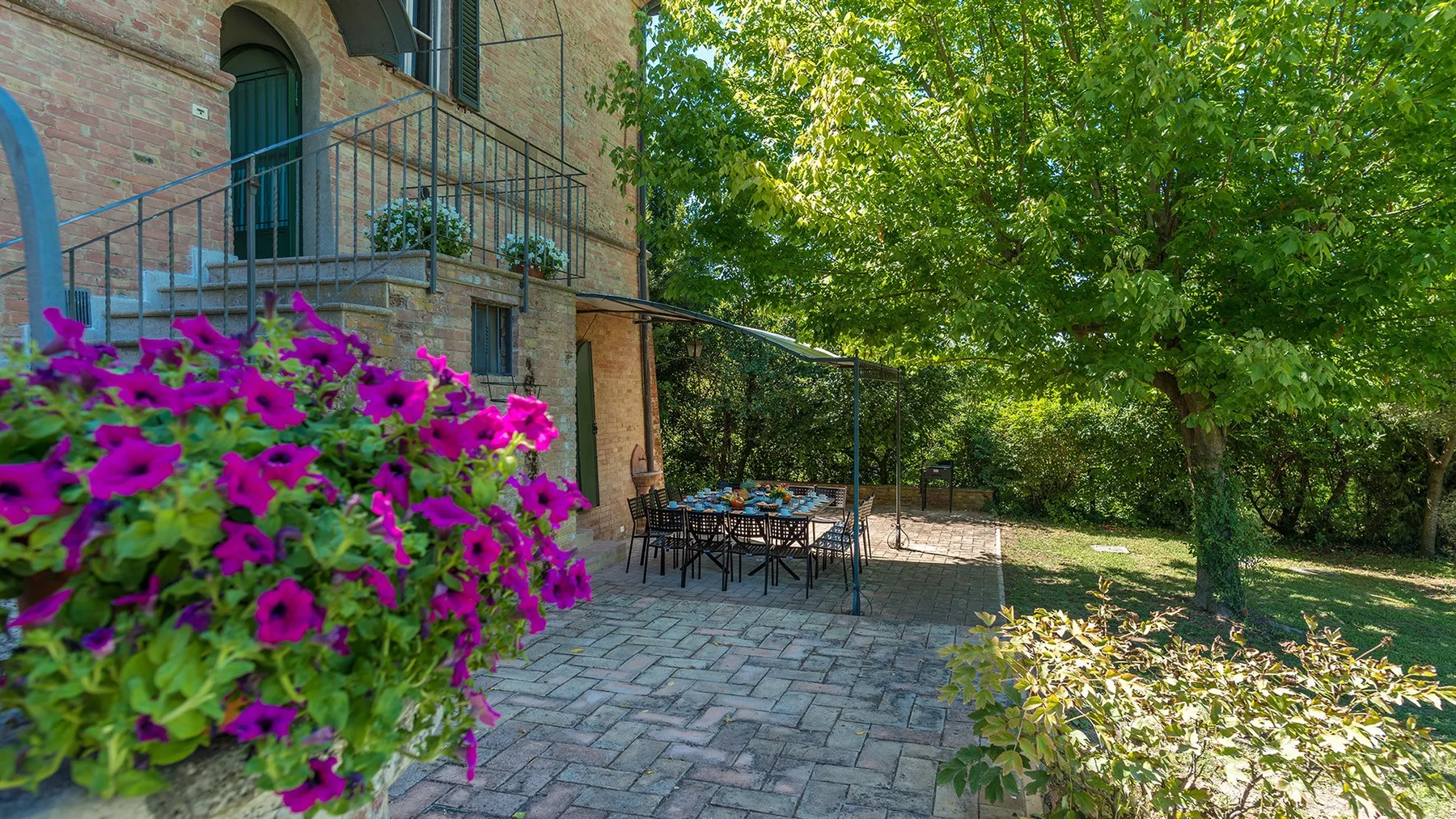 Un patio exterior junto a un edificio de ladrillo, con mesas, sillas y plantas con flores.