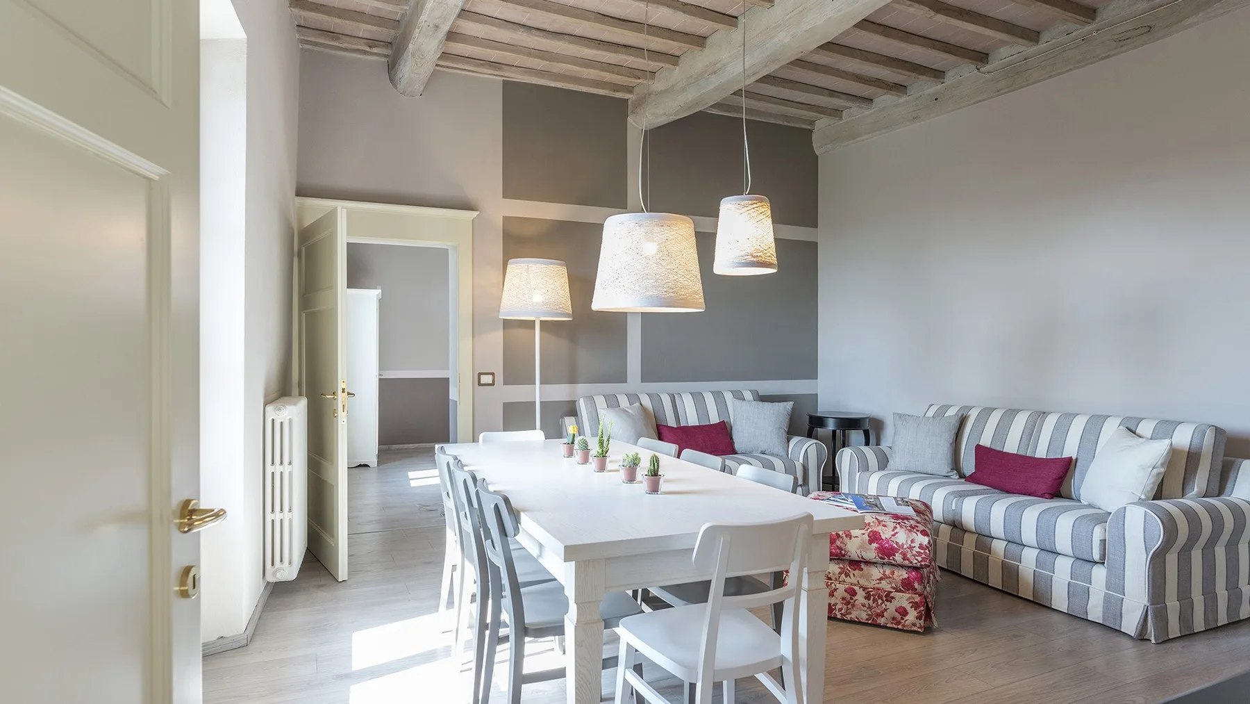 Un comedor con una mesa larga junto a asientos a rayas y lámparas colgantes.