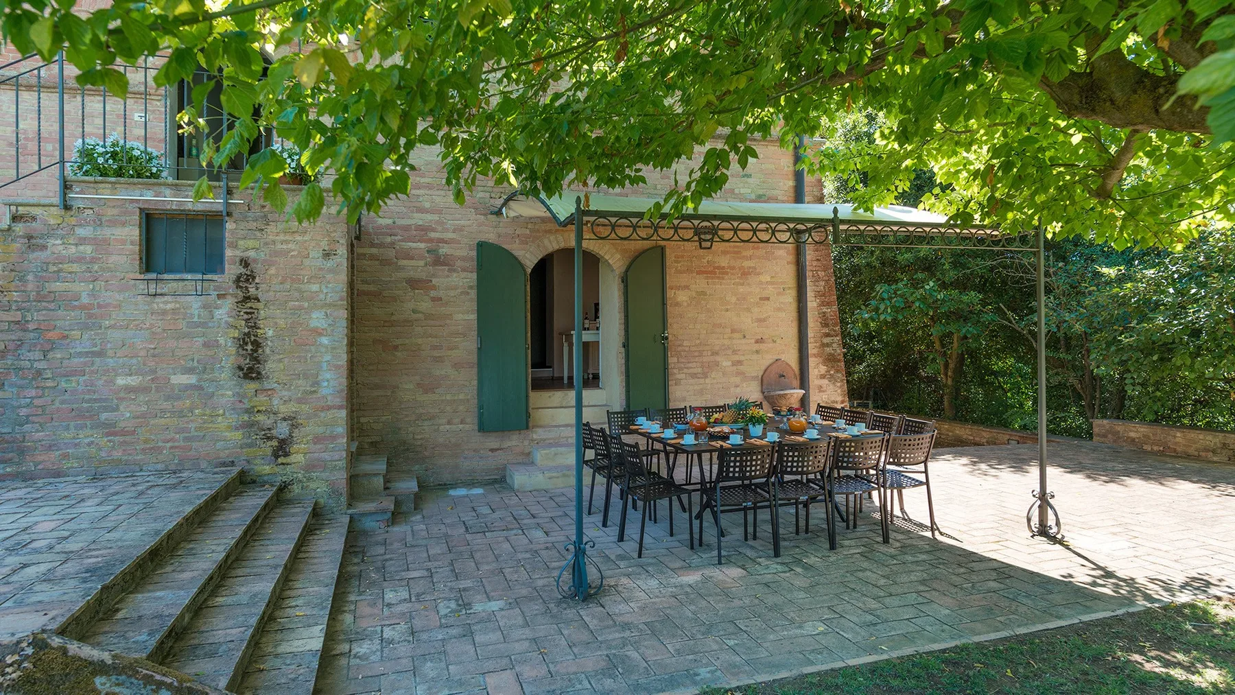 Una zona de comedor exterior a la sombra, con una mesa larga y asientos alrededor.