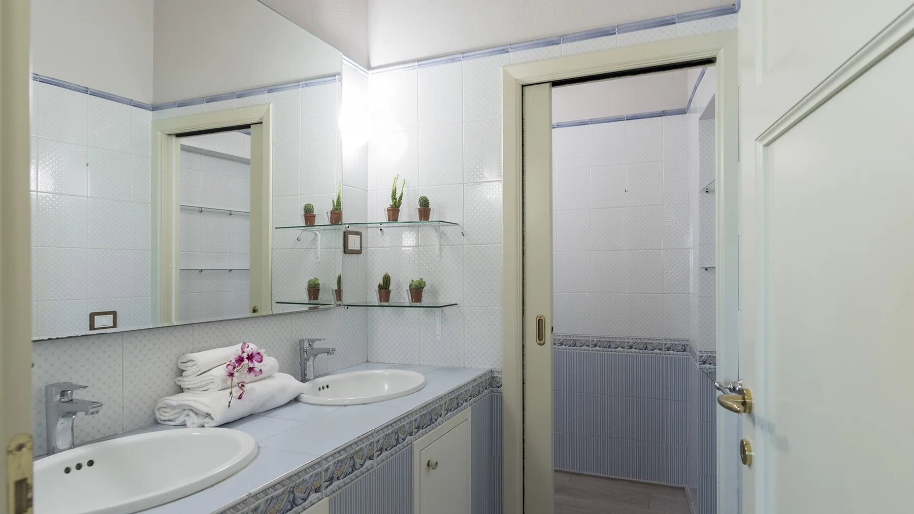 Un baño luminoso con una encimera larga, lavabos y una zona de ducha alicatada.
