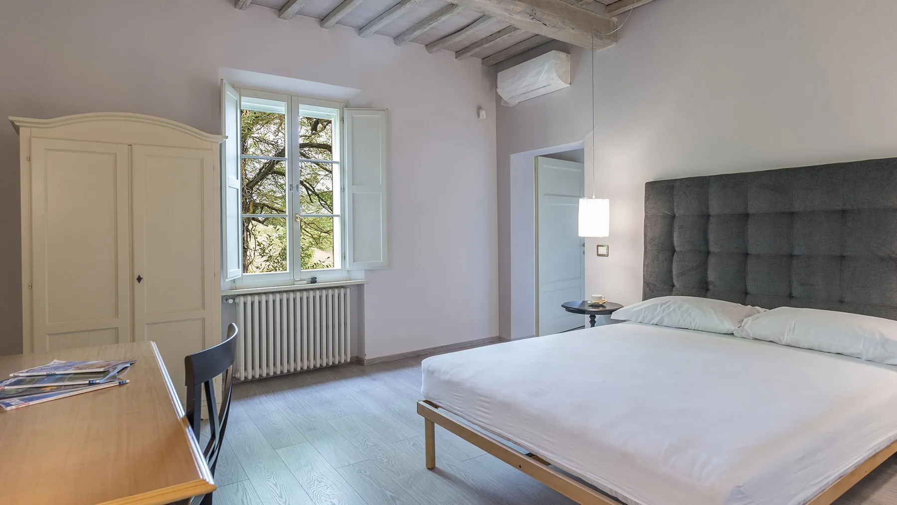 Un dormitorio con una cama grande, un armario y una ventana con vistas a los árboles.