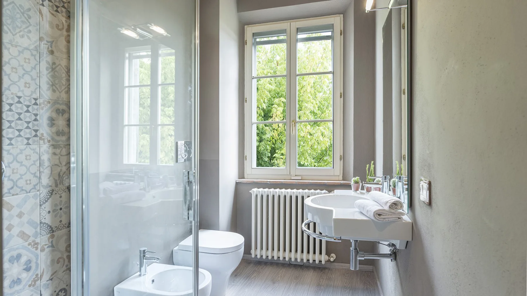 Un baño luminoso con ventana, radiador, lavabo y ducha.