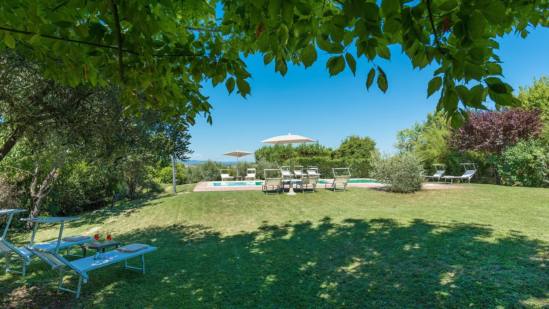 Una zona de asientos en el jardín da a una piscina, con árboles frondosos que dan sombra.