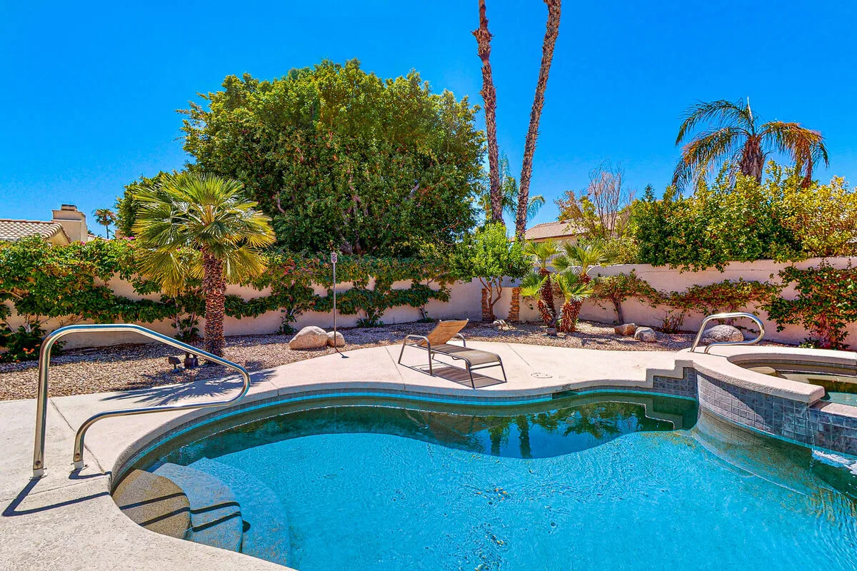 Una piscina en el patio, rodeada por un patio pavimentado y palmeras.