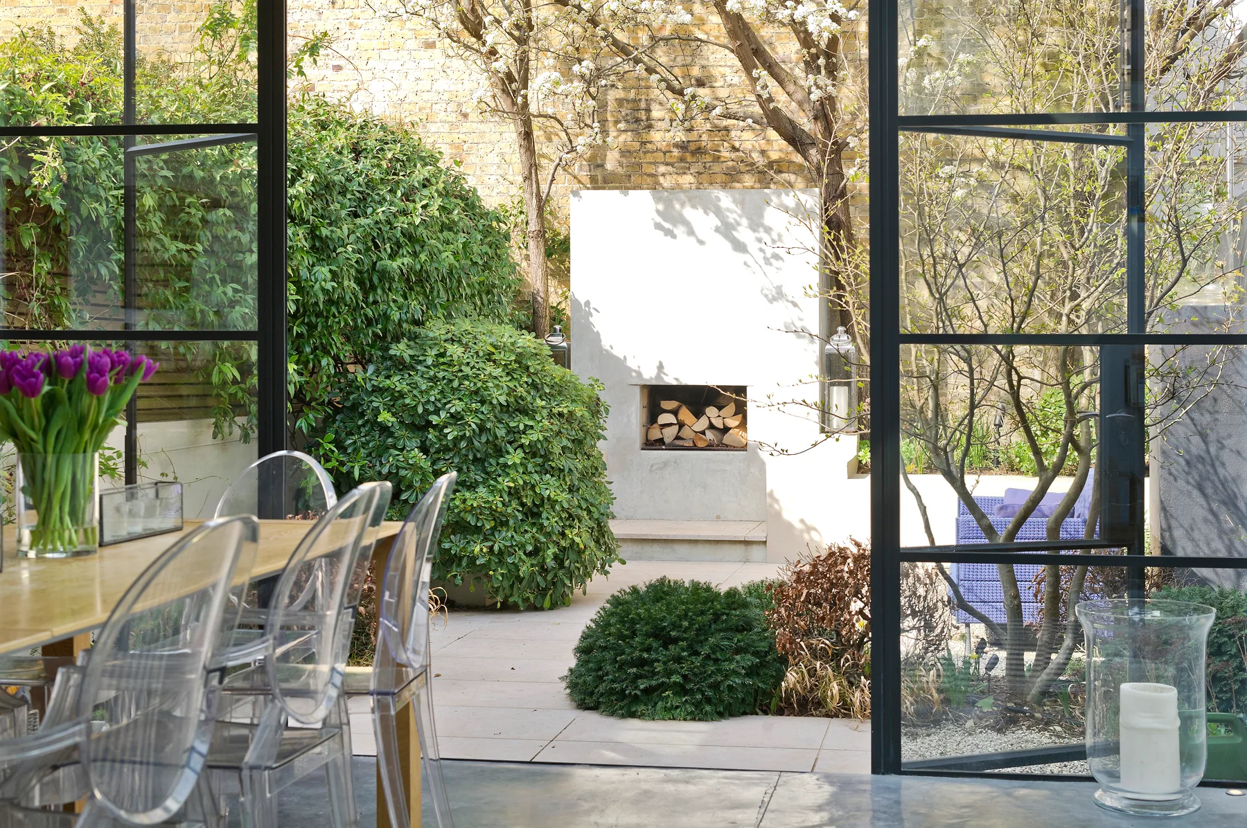 Un patio acristalado con una mesa de comedor, arbustos y una chimenea integrada.