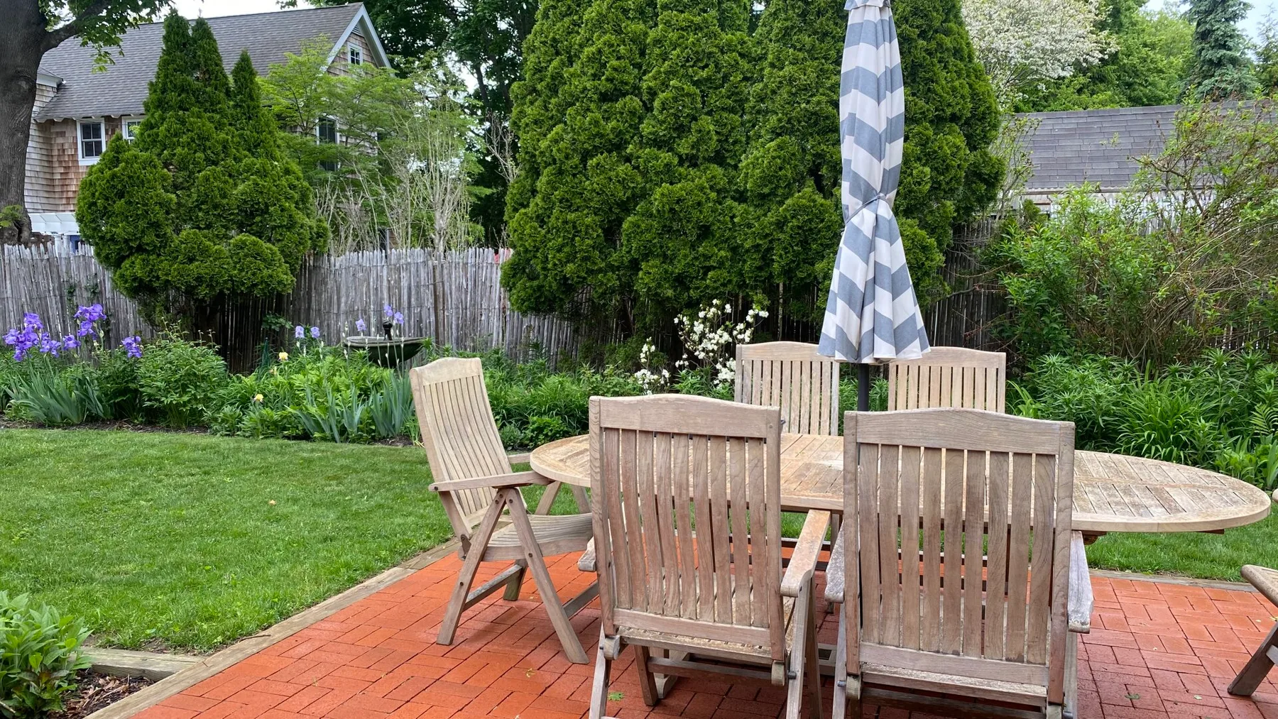 Un patio al aire libre tiene una mesa de comedor de madera, asientos y una sombrilla a rayas.