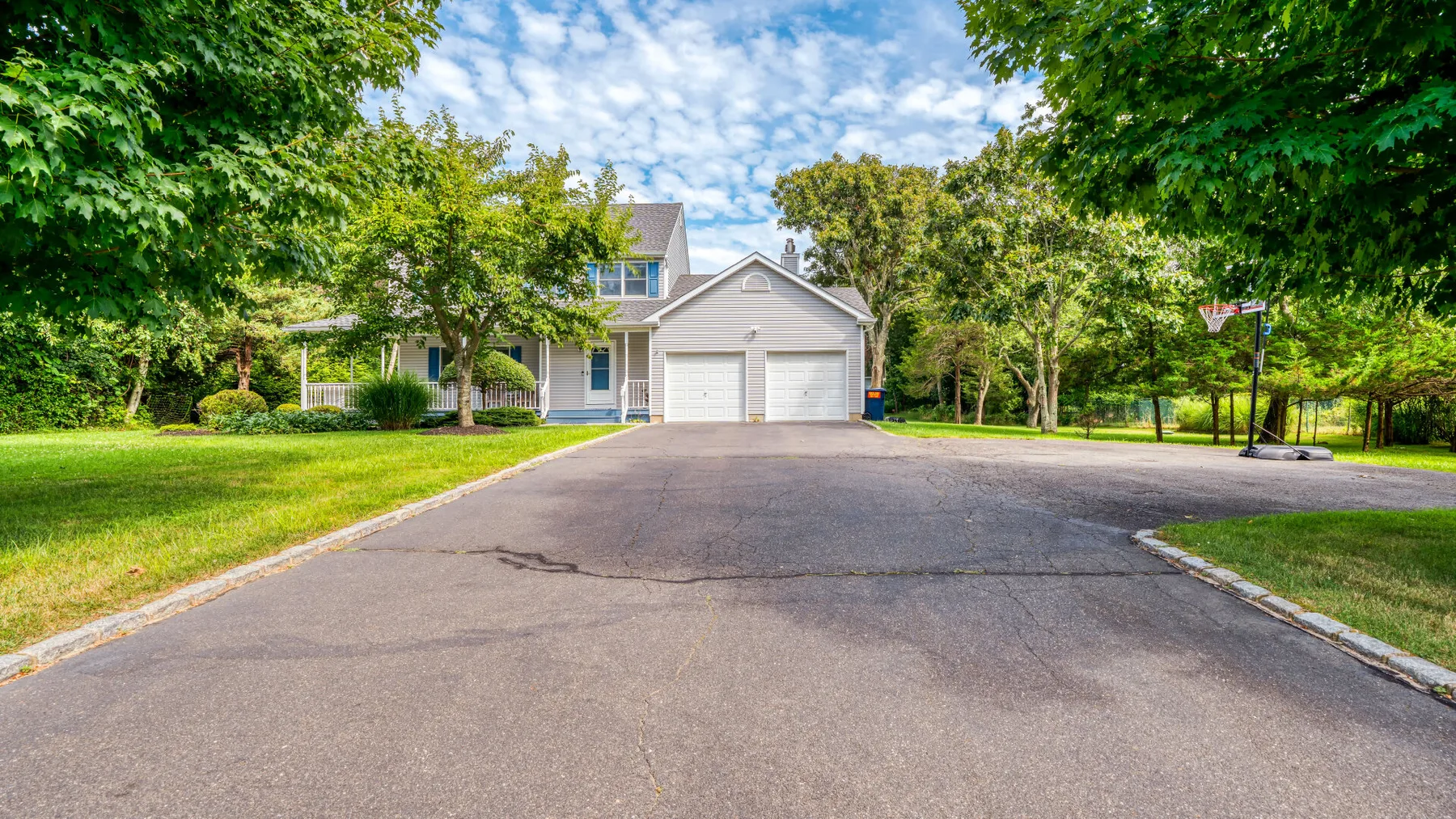 A paved driveway leads to a house with a two-car garage, surrounded by trees.