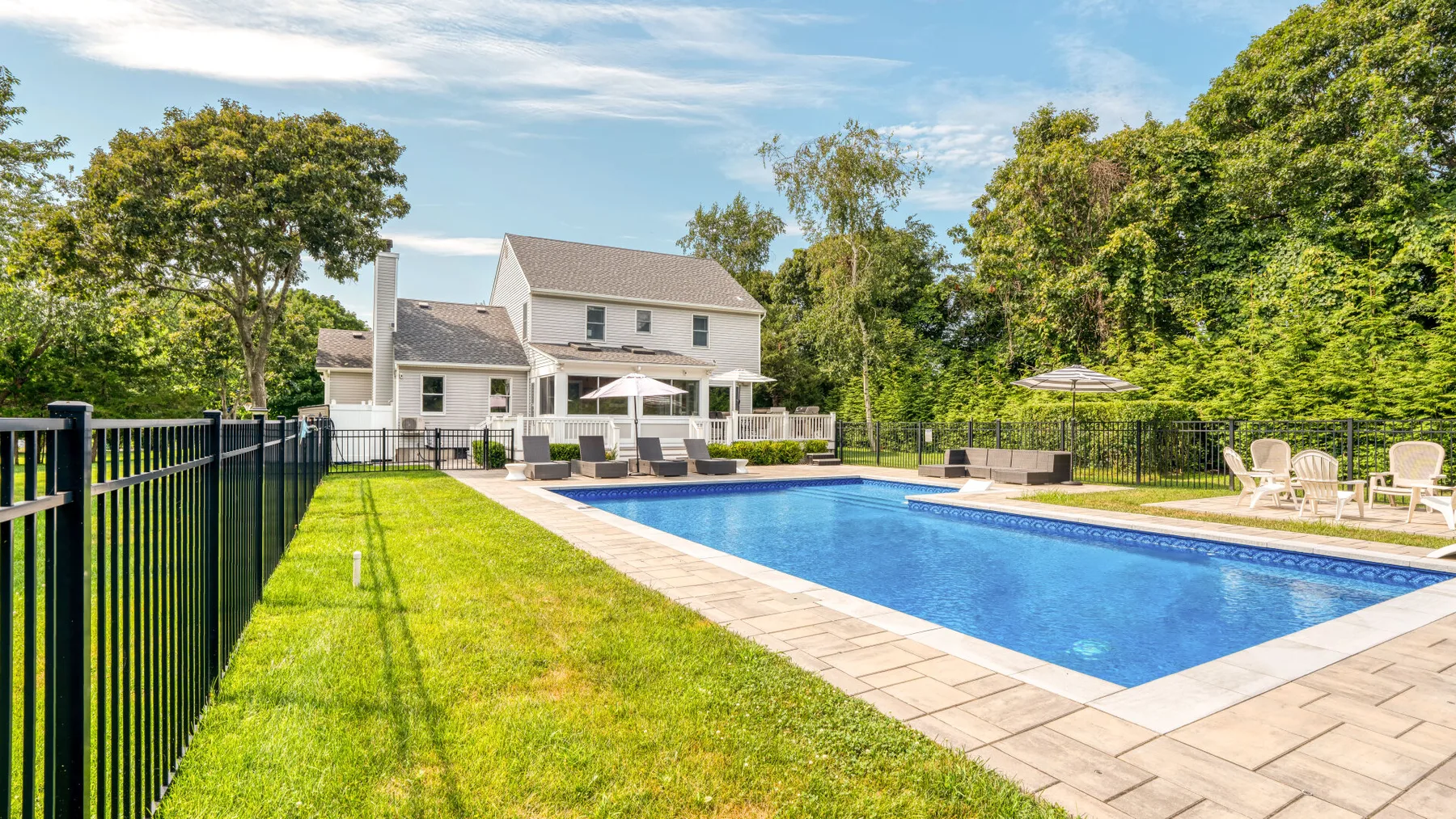 An outdoor swimming pool beside a lawn and a white house.