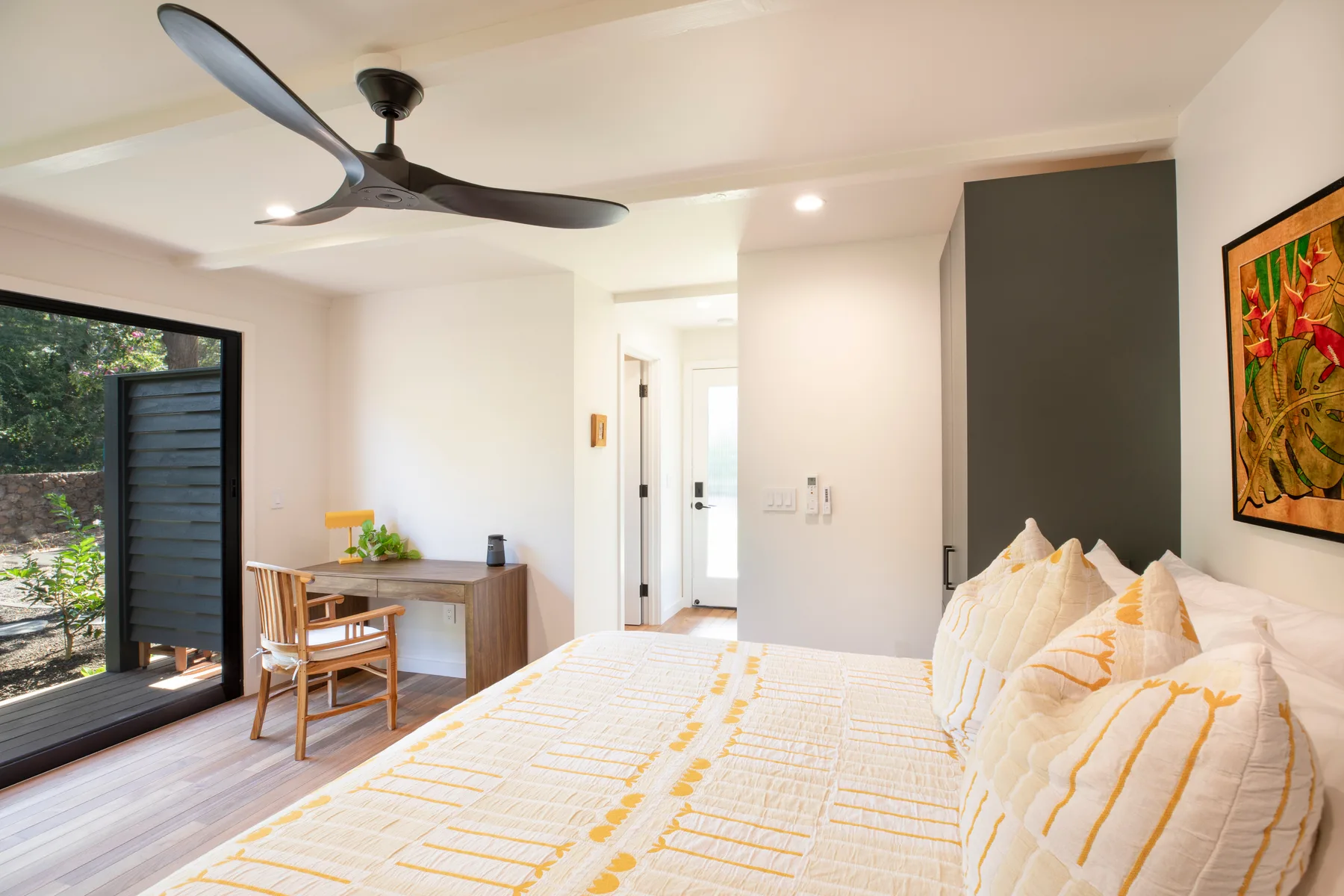 A bright bedroom with a bed, desk, and sliding glass doors opening to greenery.