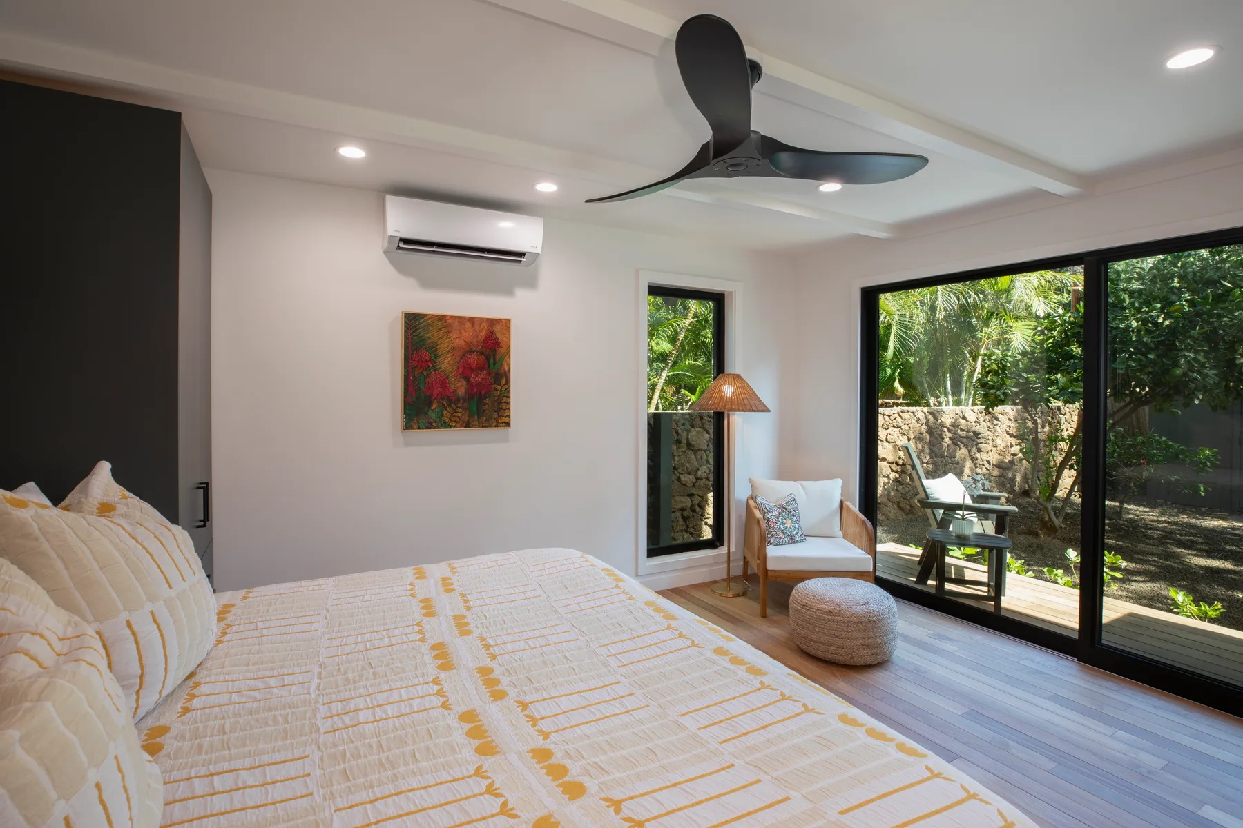 A bright bedroom with a patterned bedspread and glass doors opening to a garden.