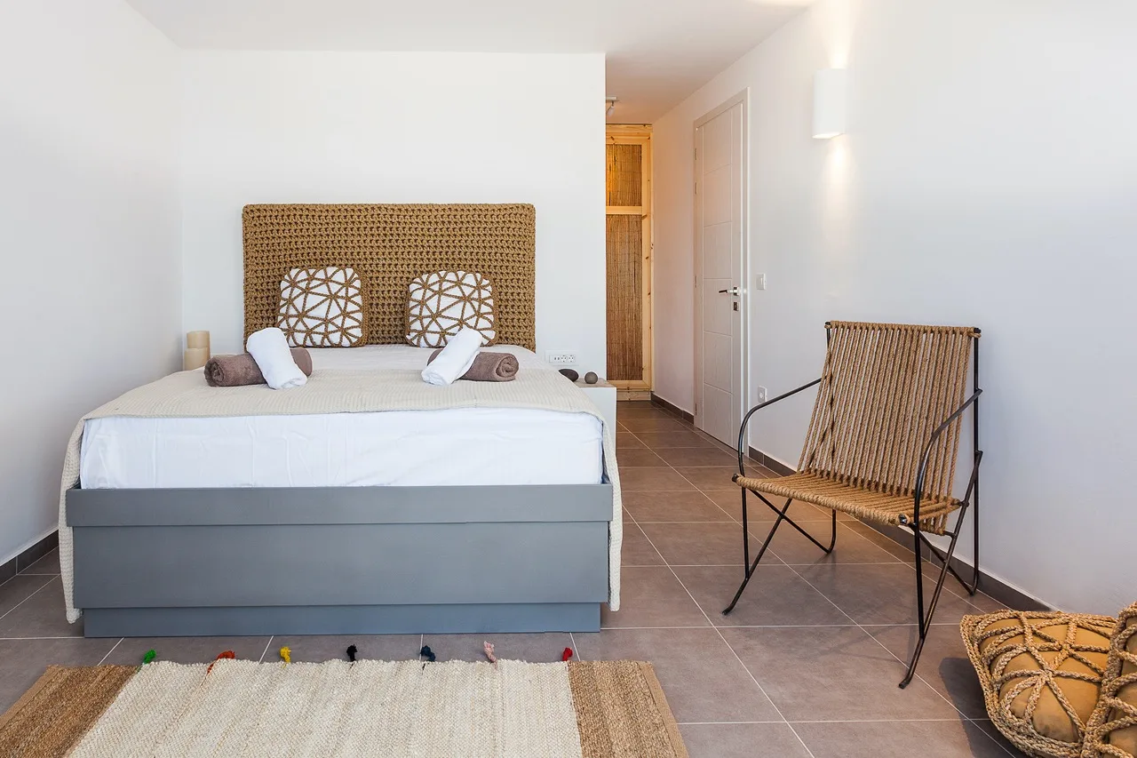 A bedroom with a neatly made bed and a woven chair beside it.