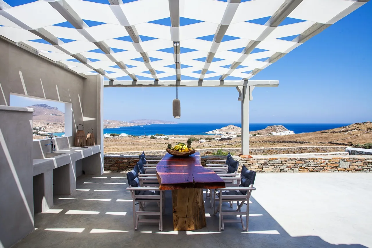 An outdoor dining area beneath a patterned canopy overlooks the sea.