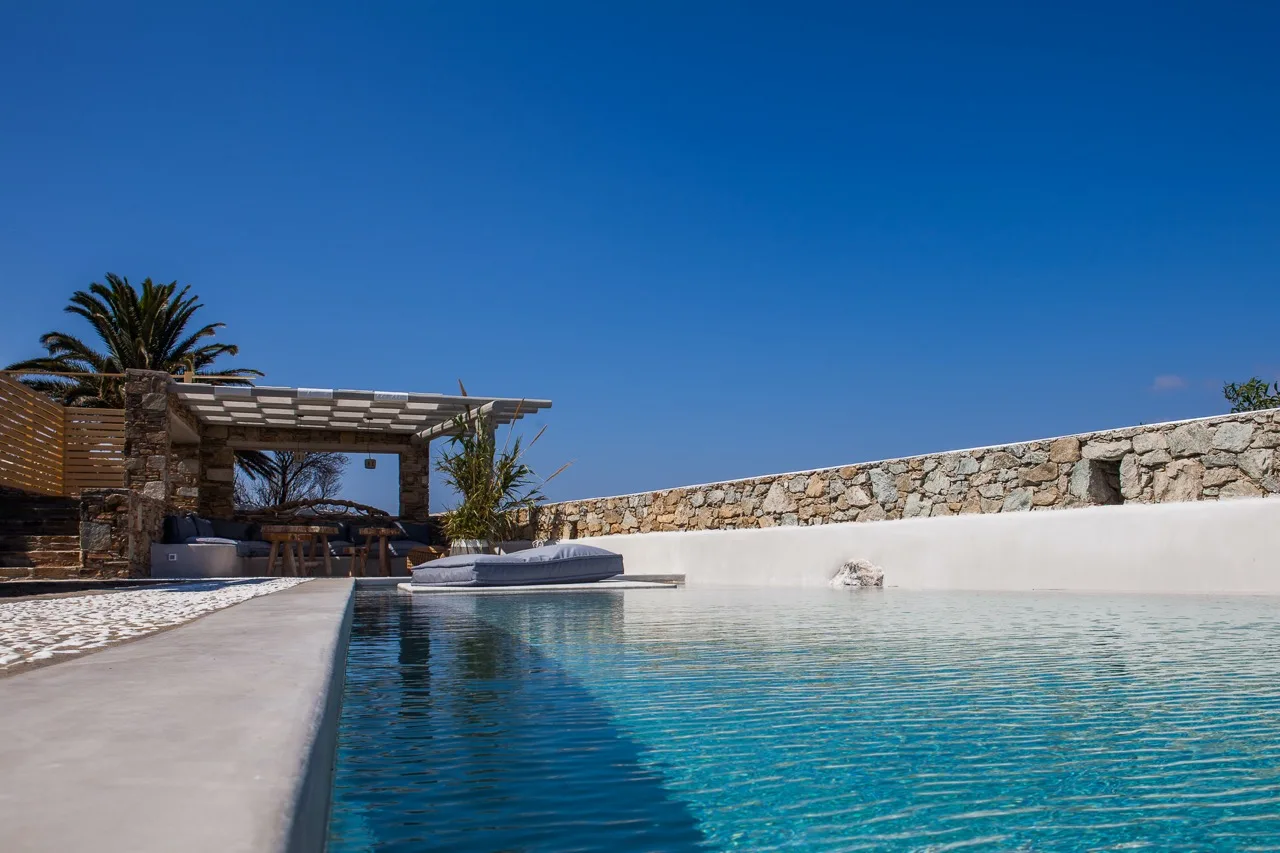 An outdoor swimming pool beside a shaded patio and stone wall.