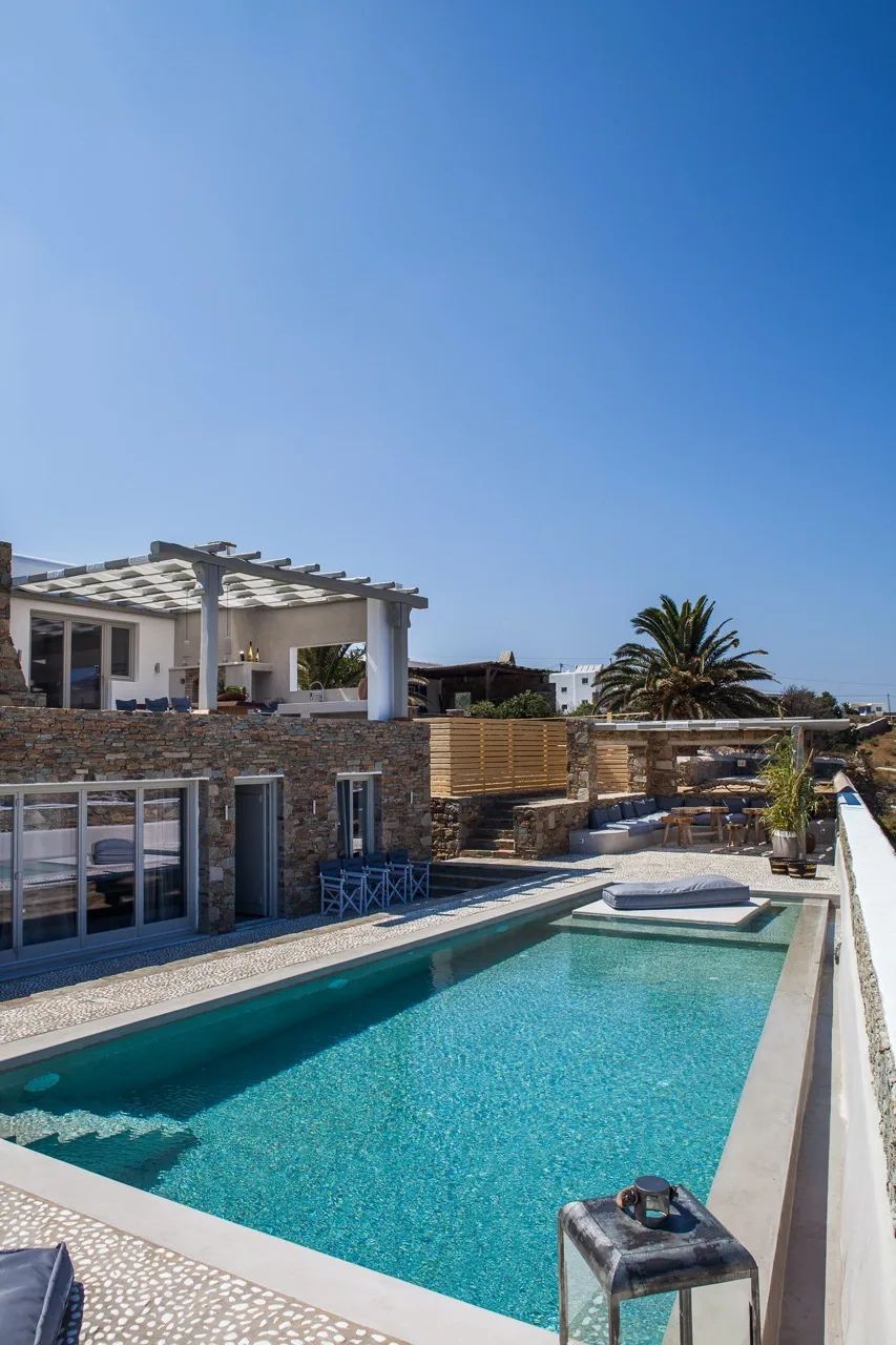 A swimming pool beside a modern building, with a palm tree in the background.