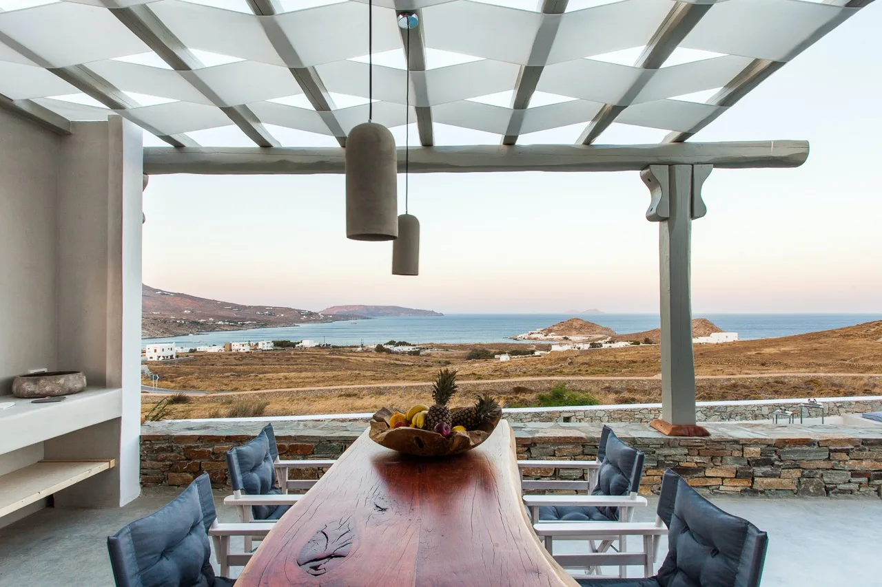 An outdoor dining area overlooks the coastline, with a long table and seating.