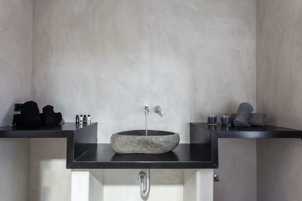 A bathroom sink sits on a dark countertop against a pale wall.