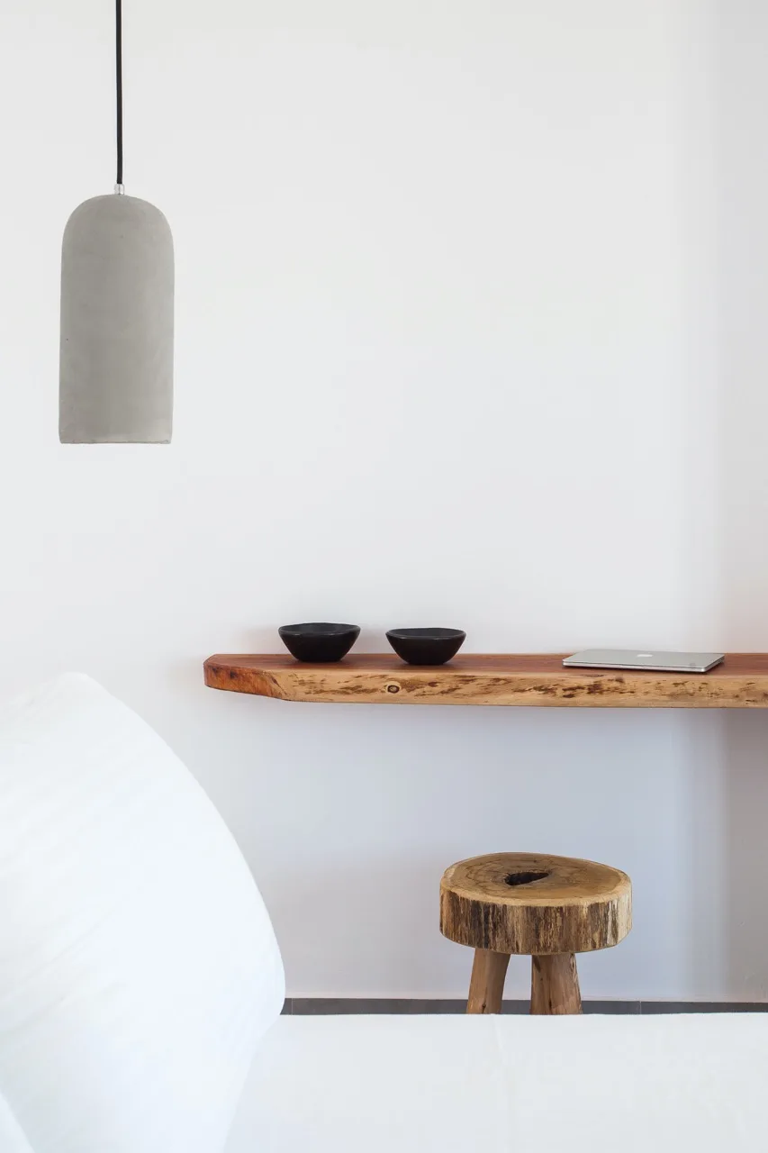 A minimalist bedroom with a wooden shelf, two bowls, and a hanging pendant light.