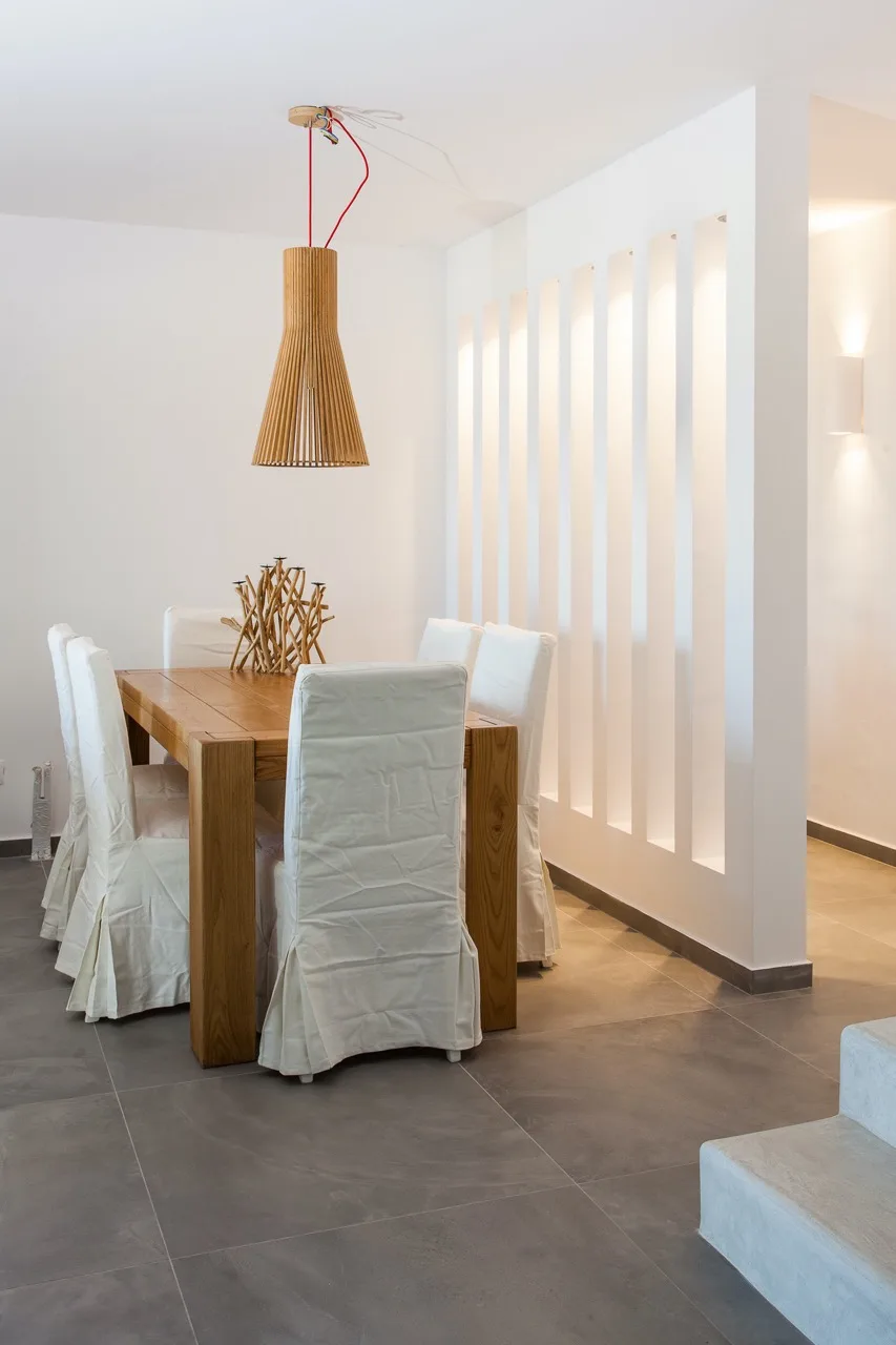 A dining area with a wooden table, white-covered seating, and a hanging pendant light.