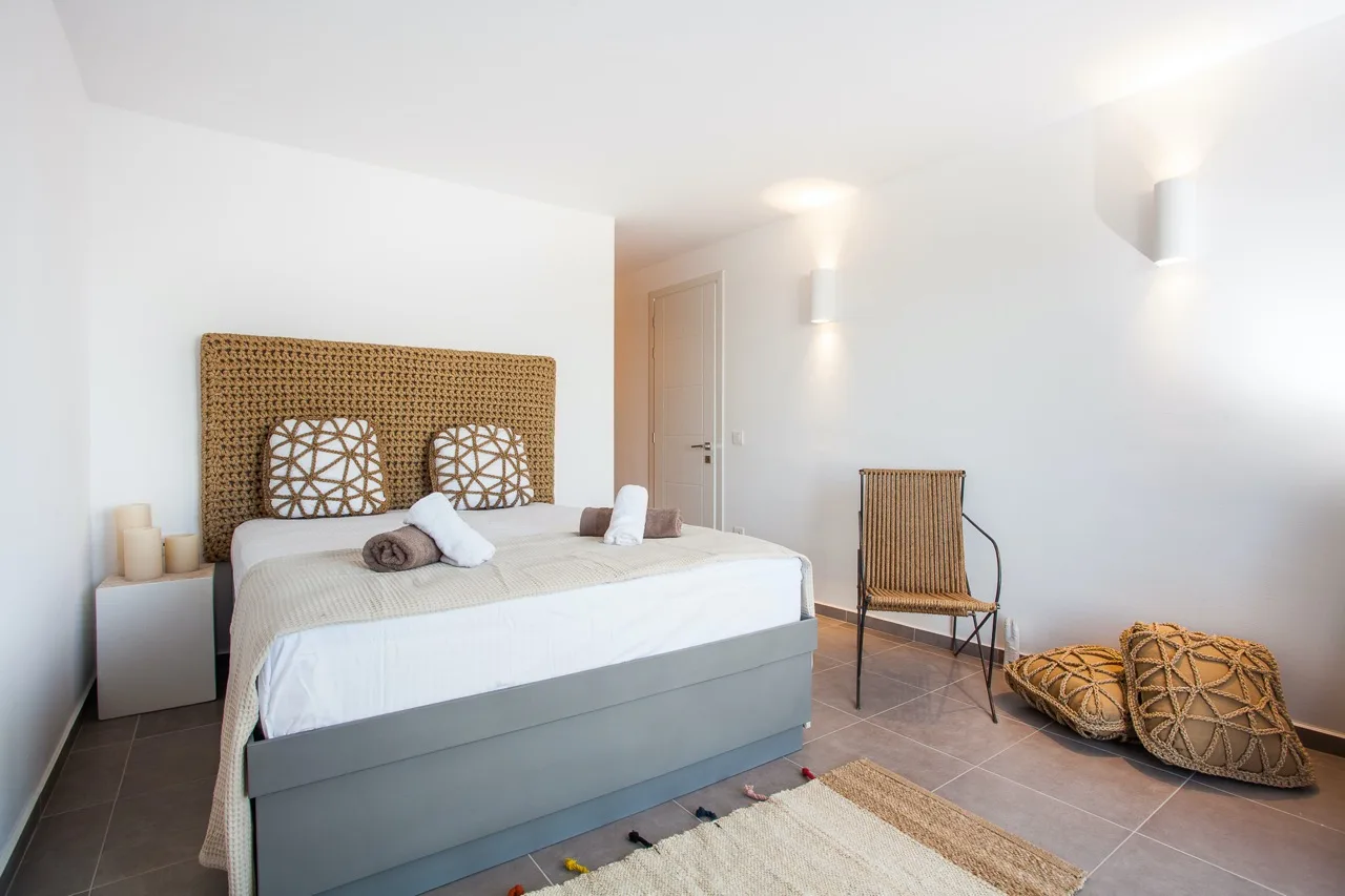 A bright bedroom with a bed, woven headboard, and chair.