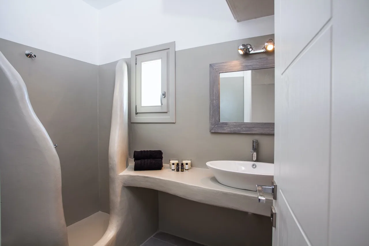 A bathroom with a curved shower area, a sink, and a wall mirror.