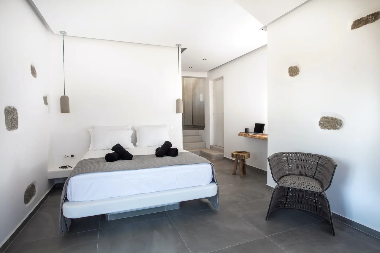 A bright bedroom with a bed, a desk, and a woven chair.