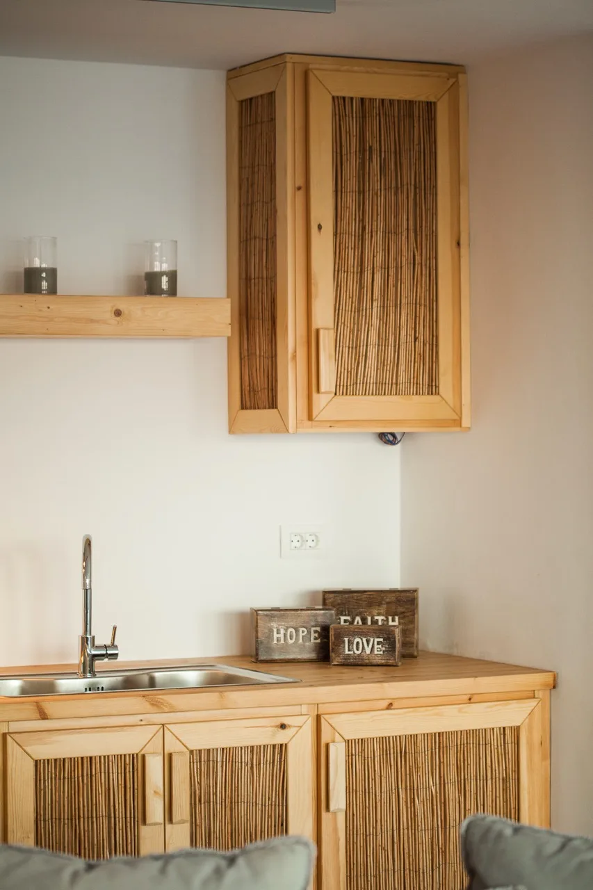 A kitchenette with a sink, wooden cabinets, and a small shelf.