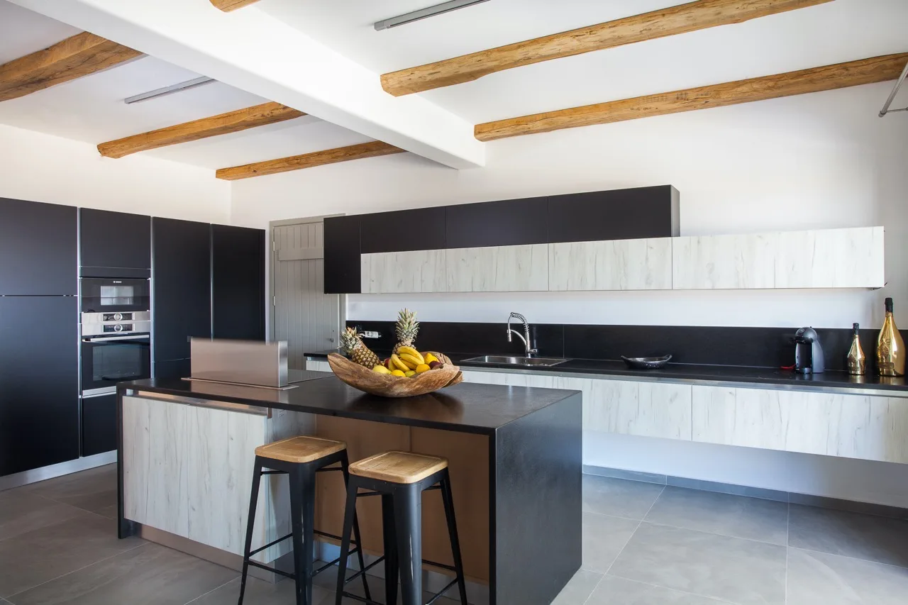 A modern kitchen with a central island, dark cabinets, and exposed wooden ceiling beams.