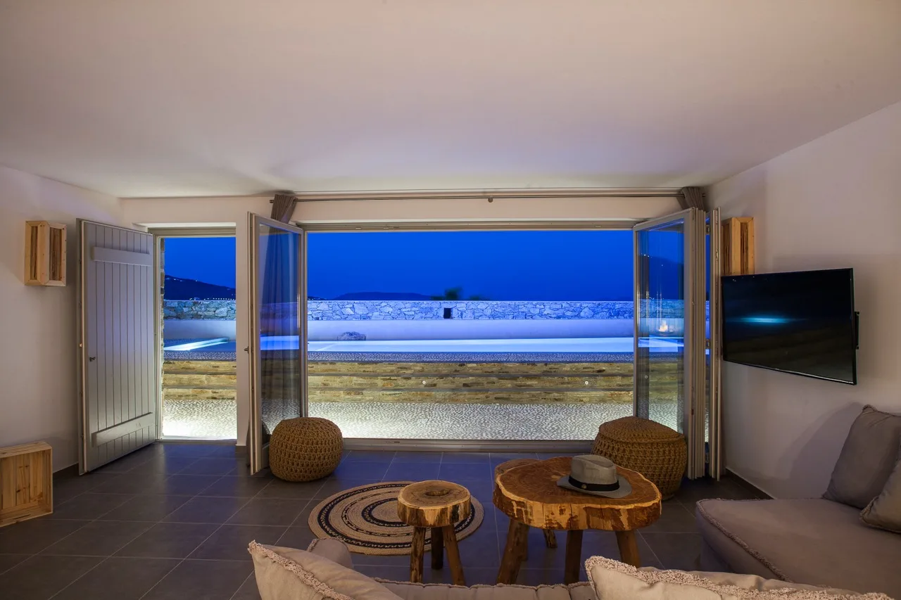 A living room opens onto a terrace with a view of the sea at dusk.