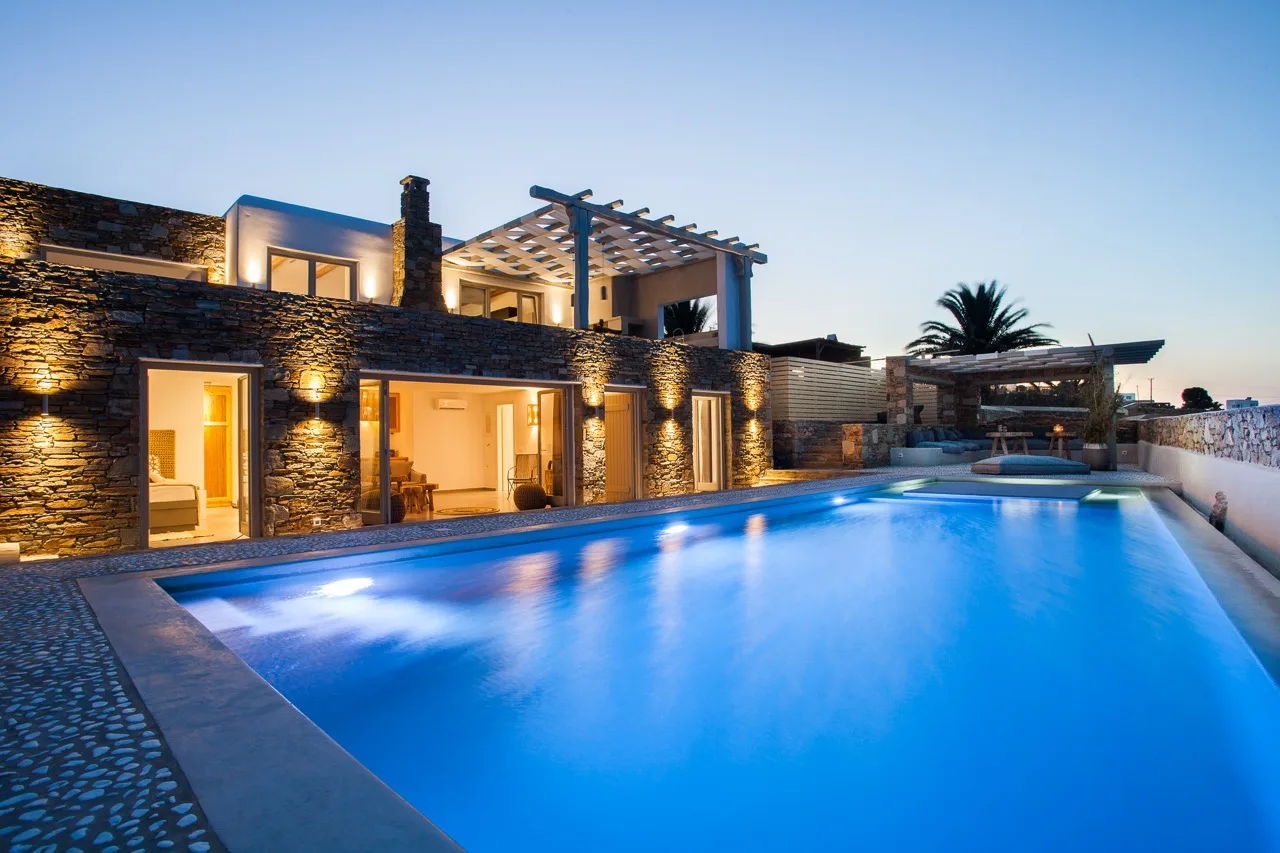 A swimming pool beside a warmly lit stone building at dusk.
