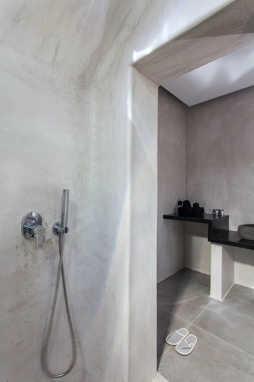 A shower area opens onto a tiled bathroom with a countertop and slippers.
