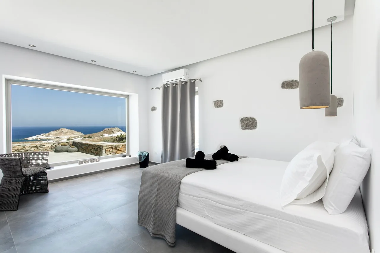 A bright bedroom with a large bed and a window overlooking the sea.