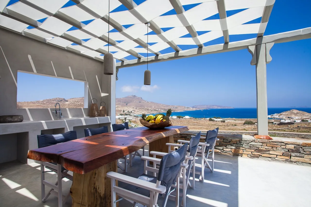 An outdoor dining area under a pergola overlooks the sea.