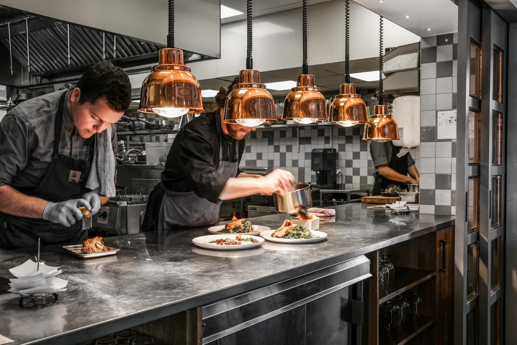 Espacio representativo del hotel: Cocineros preparan platos en una barra de cocina con lámparas colgantes de cobre.